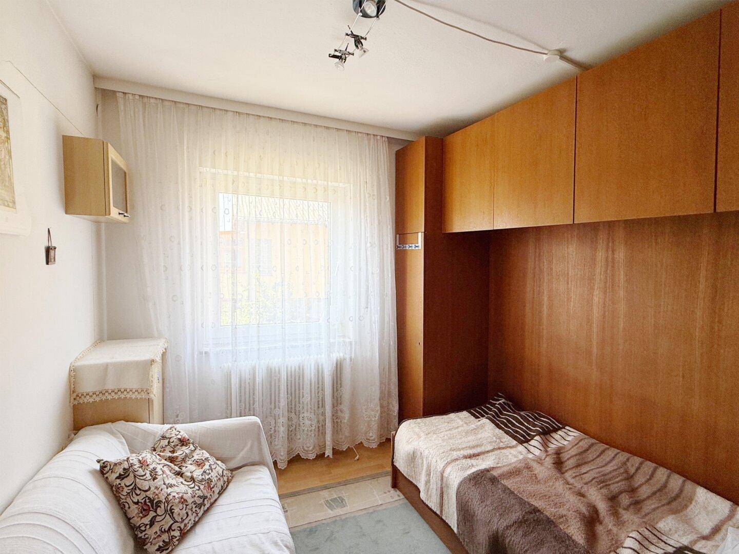 Kleines Schlafzimmer mit Einzelbett, Einbauschränken und hellem Fenster.