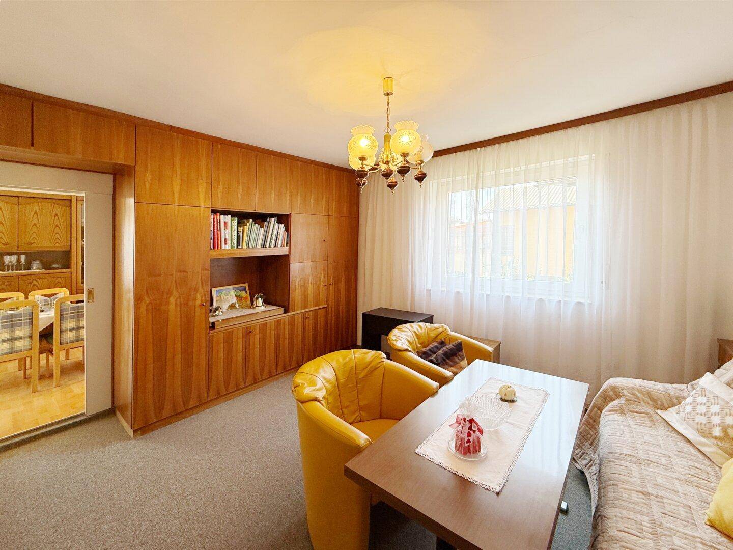 Gemütliches Wohnzimmer mit Teppichboden, Holzvertäfelung und gelben Sesseln.
