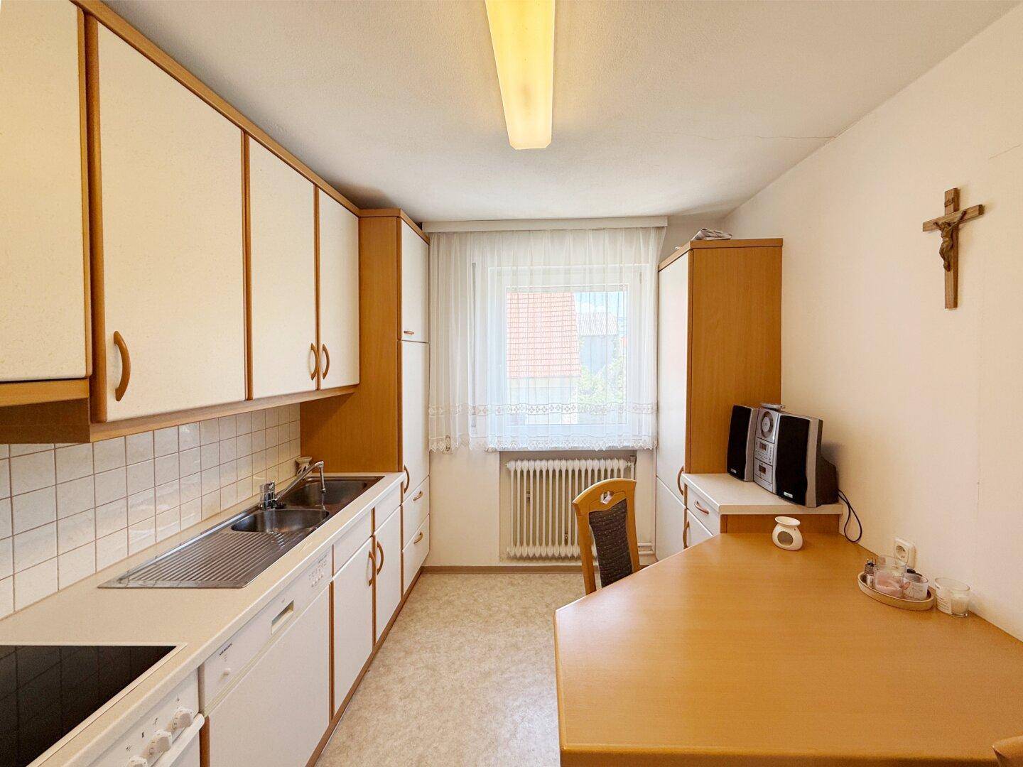 Funktionale Küche mit weißen Schränken, Essbereich und Fenster.