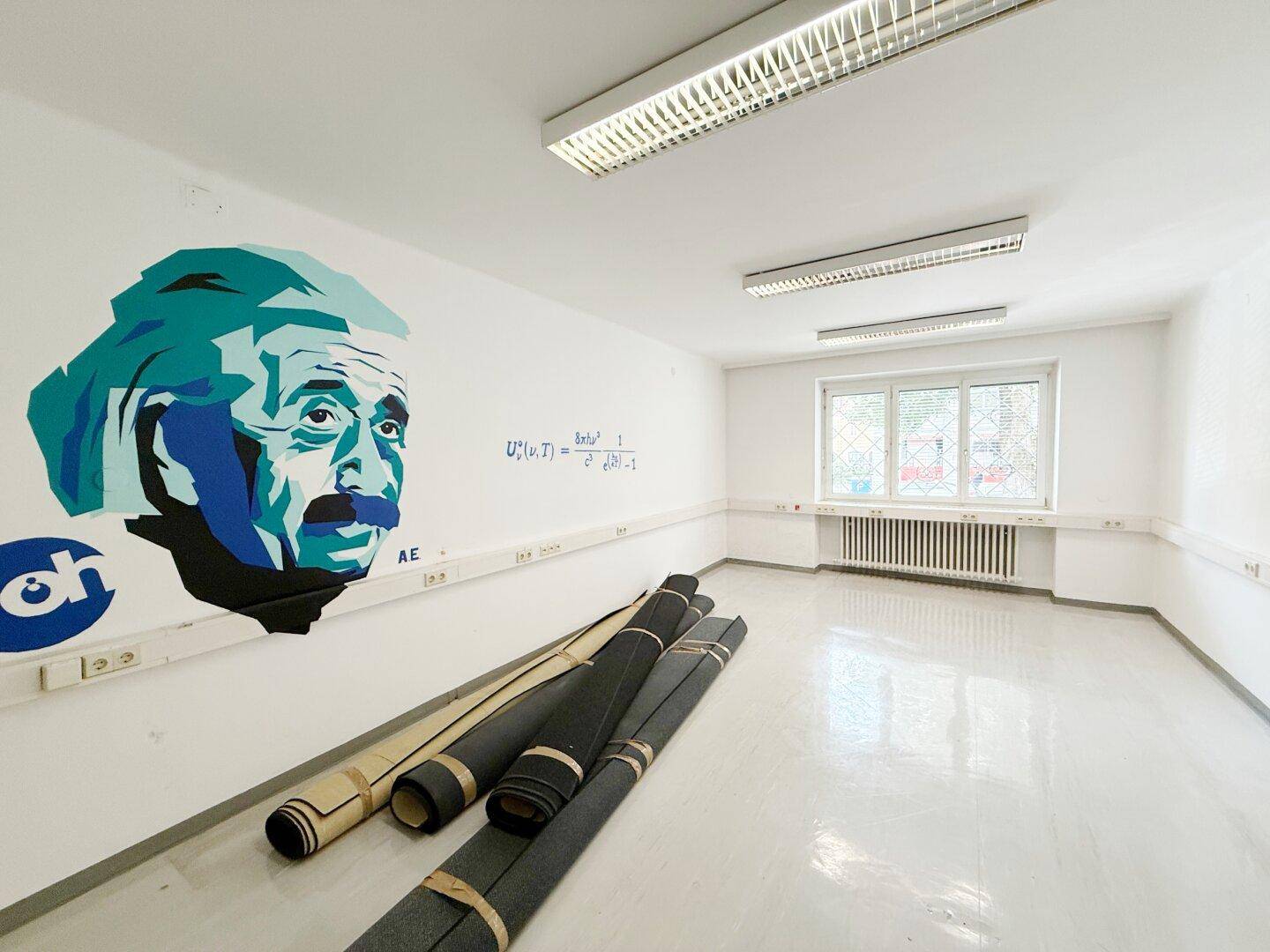Geräumiger Büroraum mit Einstein-Wandgemälde, großen Fenstern und glänzendem Boden.