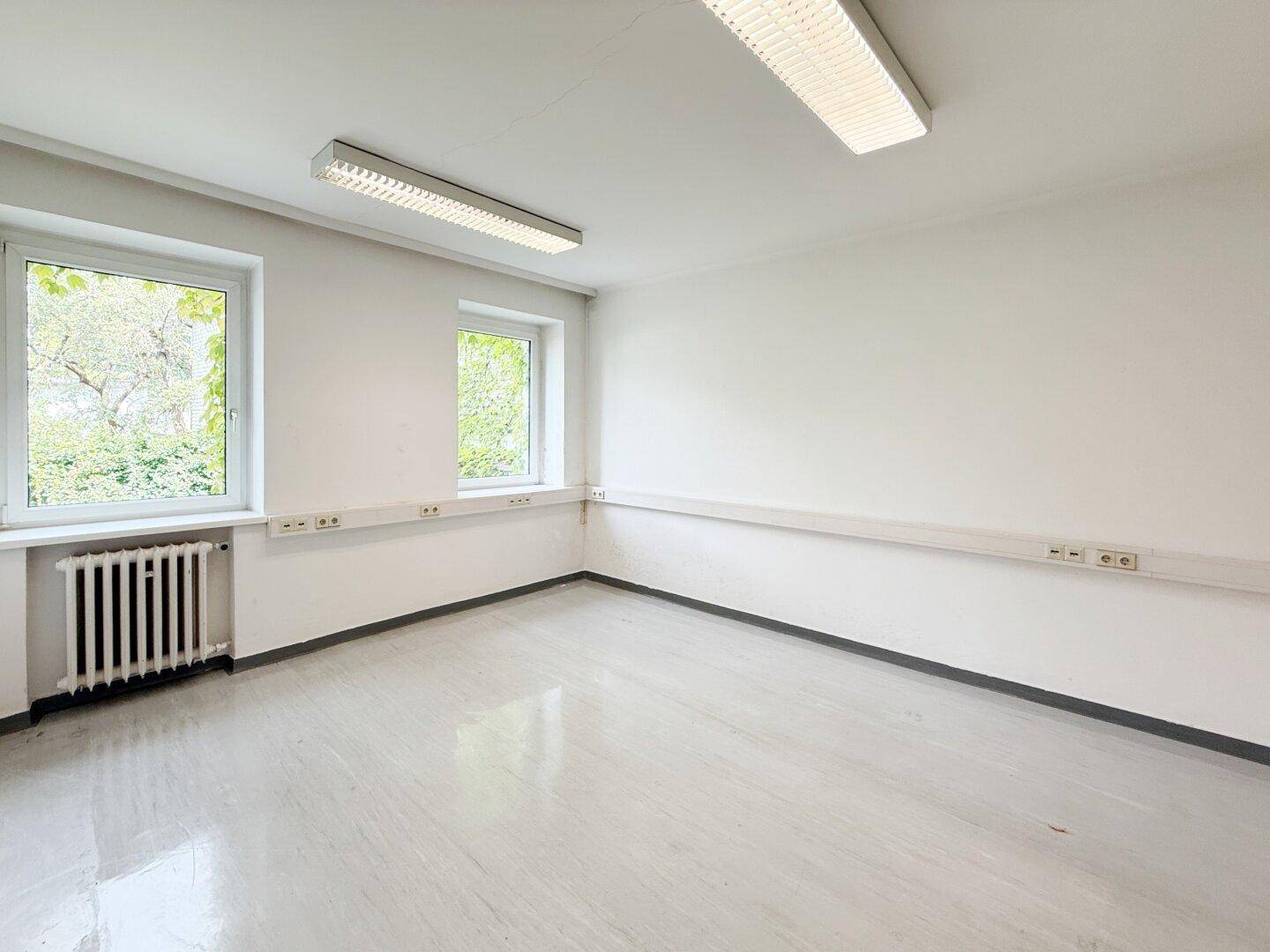 Heller Büroraum mit zwei Fenstern, weißen Wänden und glänzendem Boden.