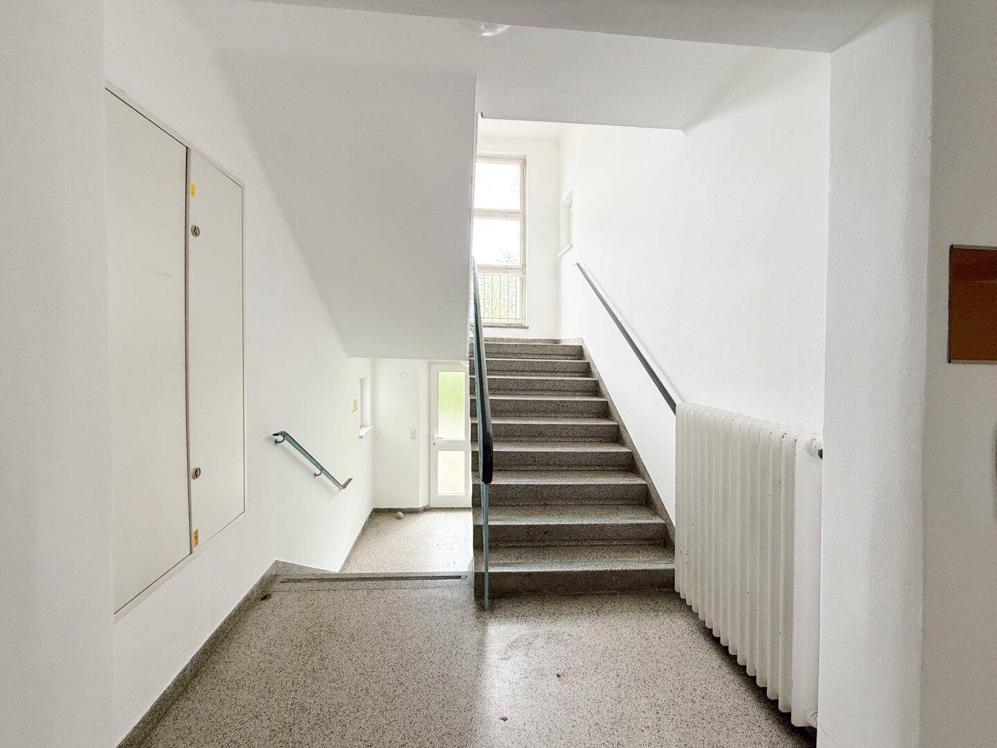 Treppenhaus mit Terrazzoboden, weißen Wänden und Geländer.