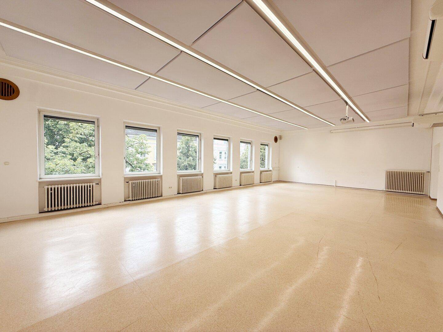 Geräumiger Büroraum mit vielen Fenstern, abgehängter Decke und Projektor.