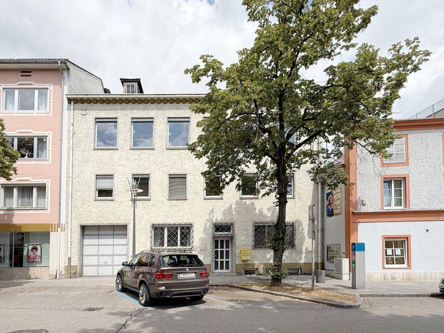 Ansicht der Gebäudefassade von der Straße mit parkendem Auto und Bäumen.