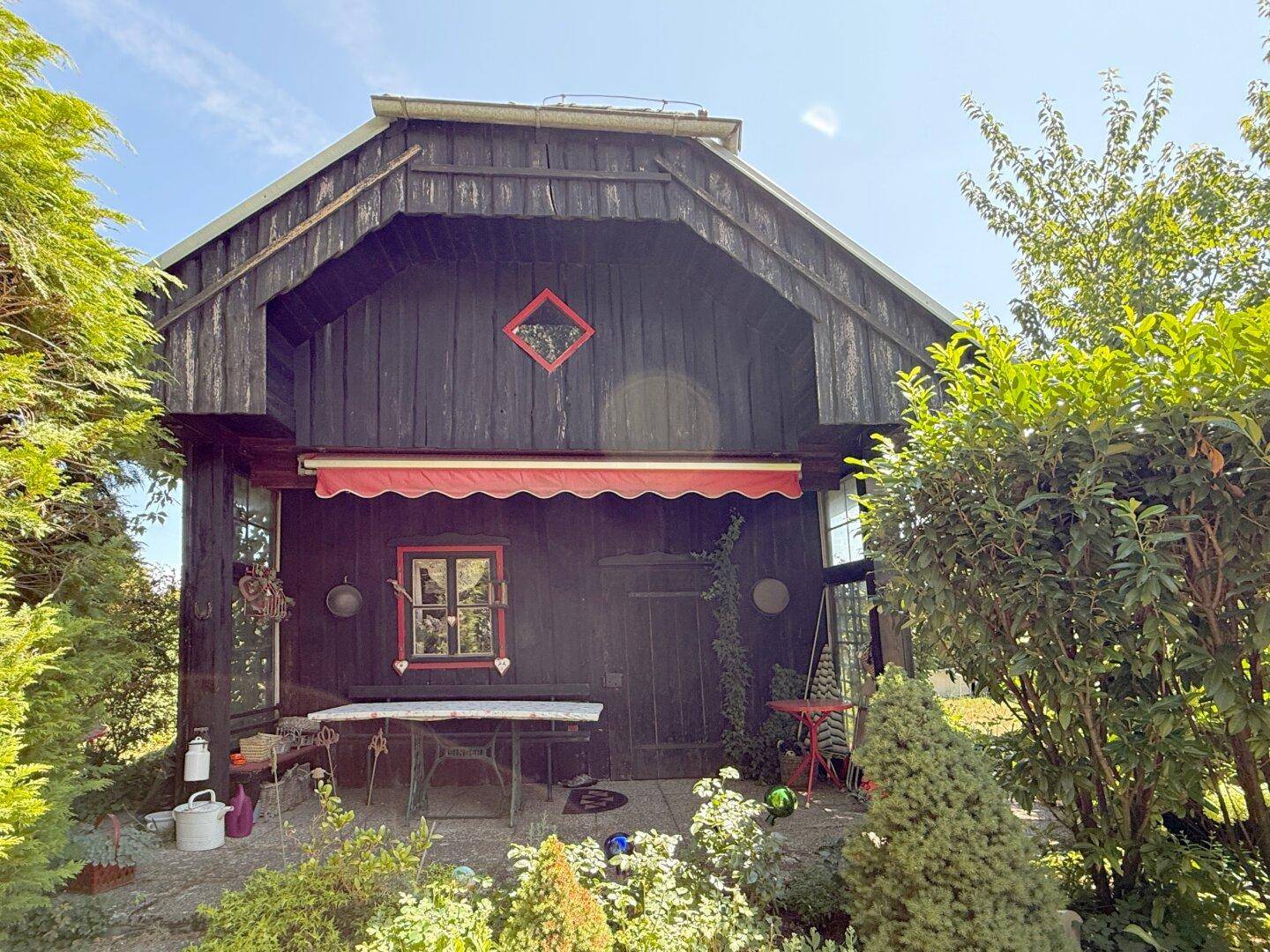 Gemütliche Terrasse vor dem Holzhaus mit Tisch und Stühlen, geschützt durch eine rote Markise.