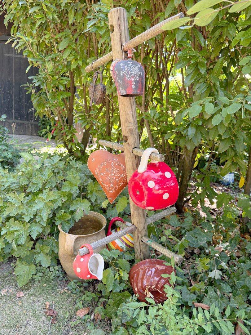 Detailansicht von rustikalen Gartendekorationen aus Keramik und Holz inmitten grüner Pflanzen.
