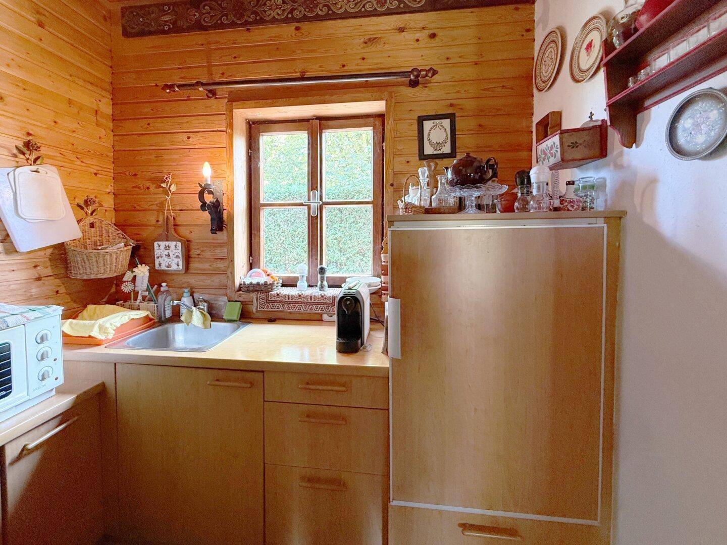 Kleine, funktionale Küchenzeile mit Holzfronten, Spüle und Kühlschrank in rustikalem Ambiente.