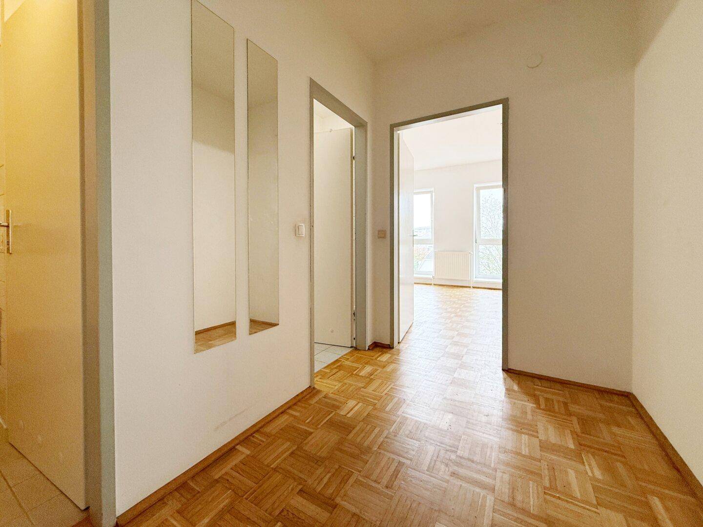 Heller Flur mit Parkettboden und integrierten Spiegeln, führt zu weiteren Räumen.