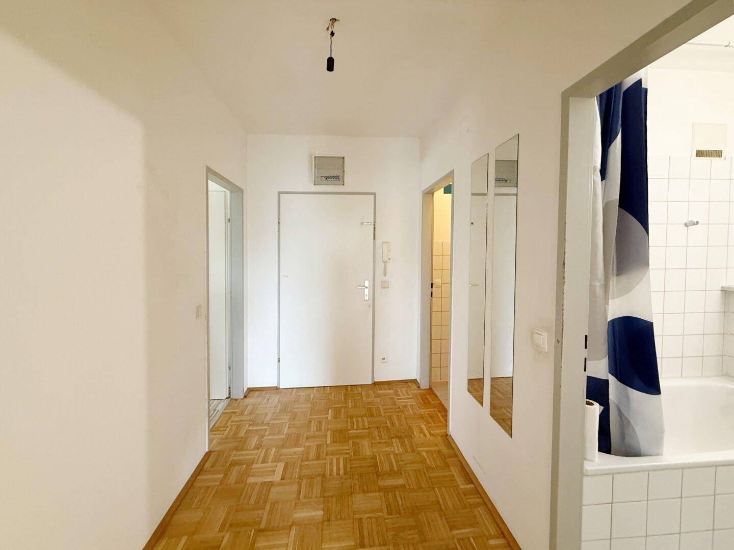 Flur mit Parkettboden, mehreren Türen und Blick ins Badezimmer.