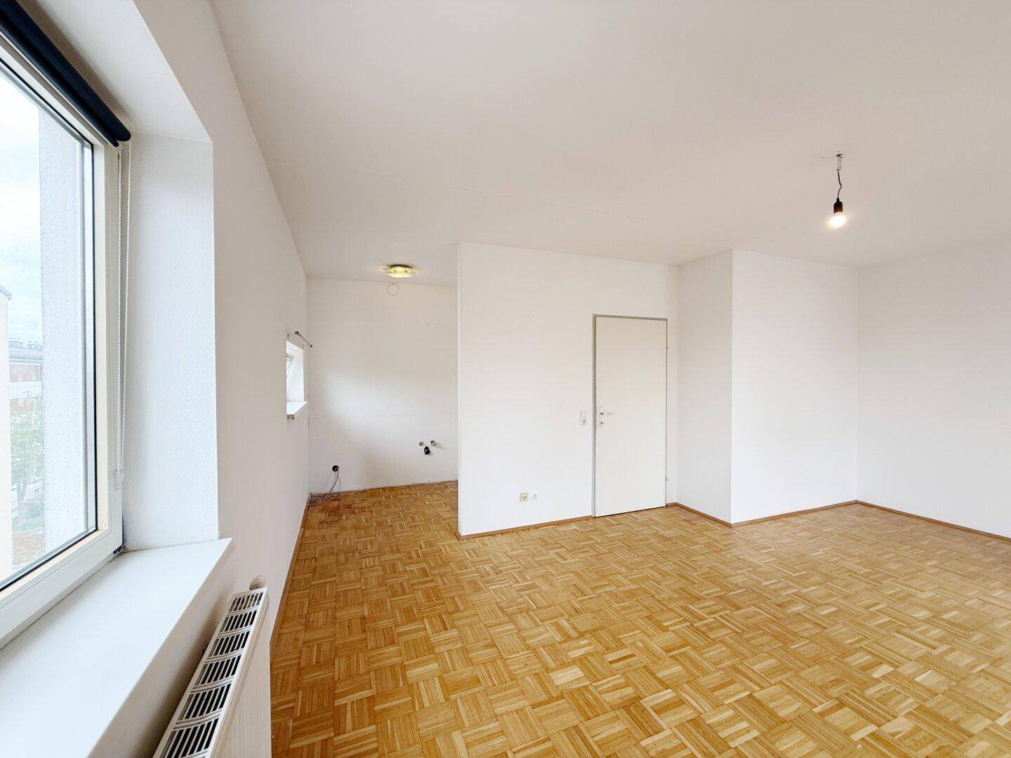 Leerer Raum mit Parkettboden und Anschlüssen für eine Küche.