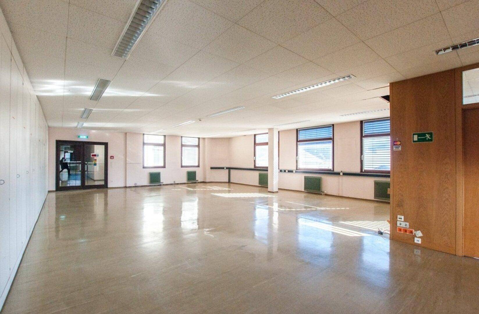Helles, leeres Büro mit mehreren Fenstern, die viel Tageslicht hereinlassen, und einem glänzenden hellen Boden.