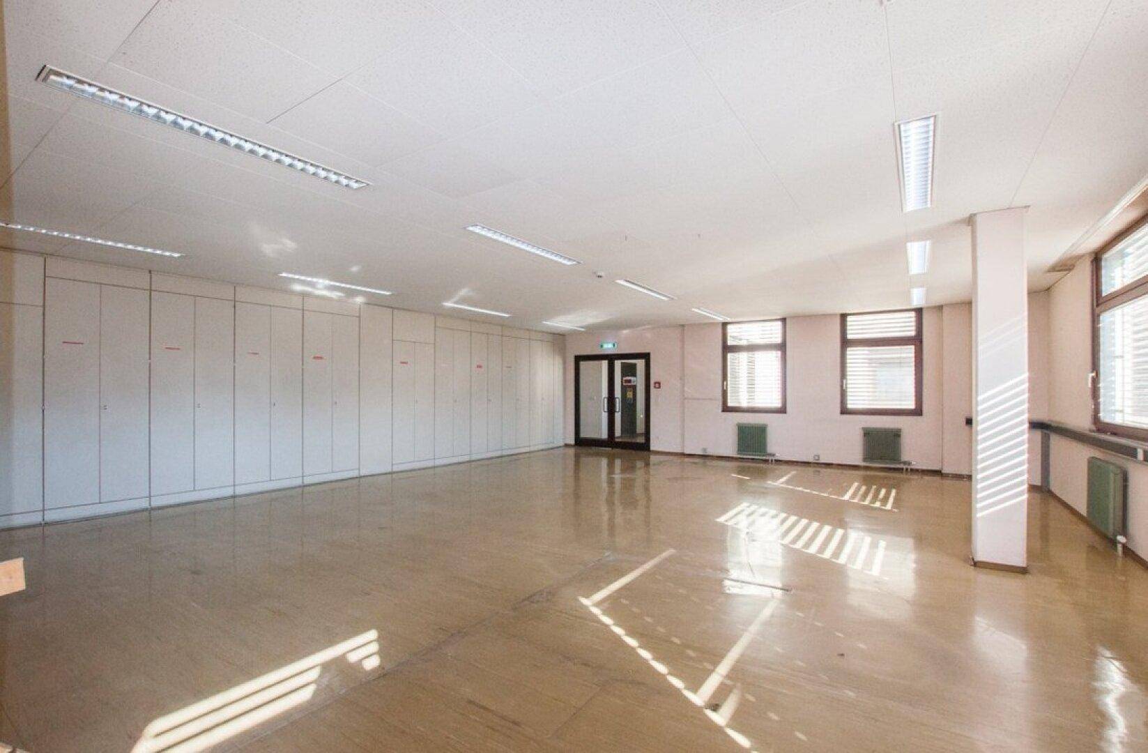 Geräumiges Büro mit hellem Steinboden, Einbauschränken und großen Fenstern, die viel Tageslicht hereinlassen.