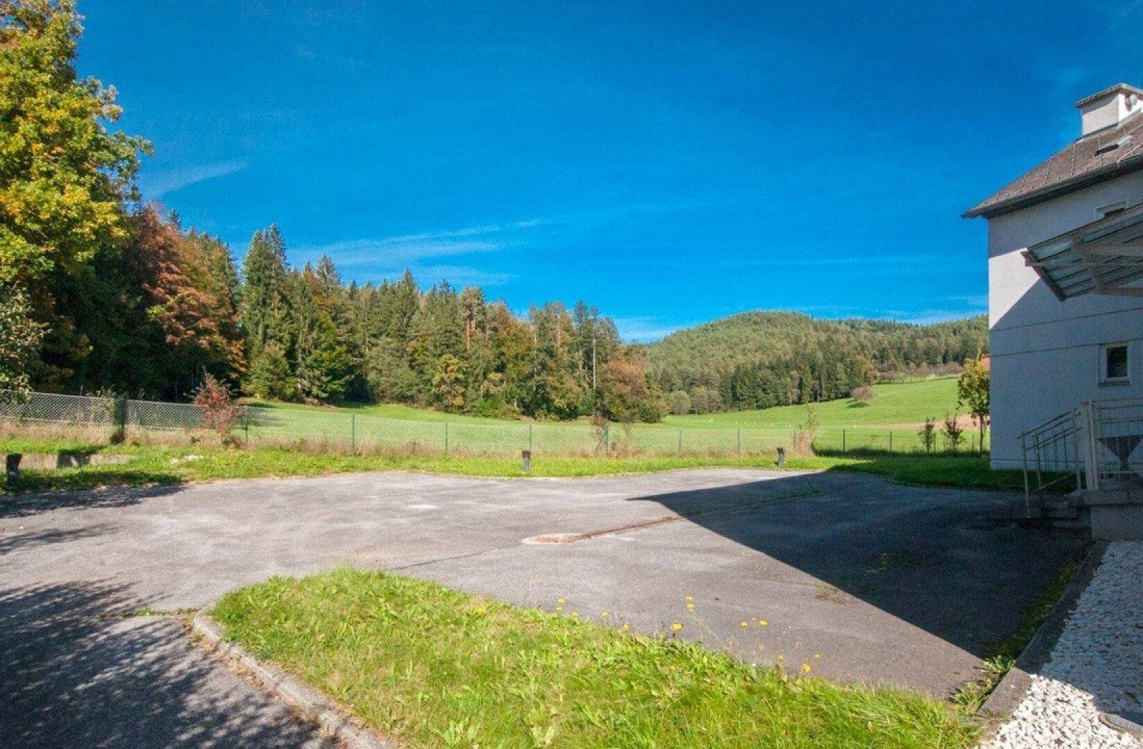 Großer asphaltierter Parkplatz neben dem Gebäude mit weitem Blick auf die grüne Landschaft.