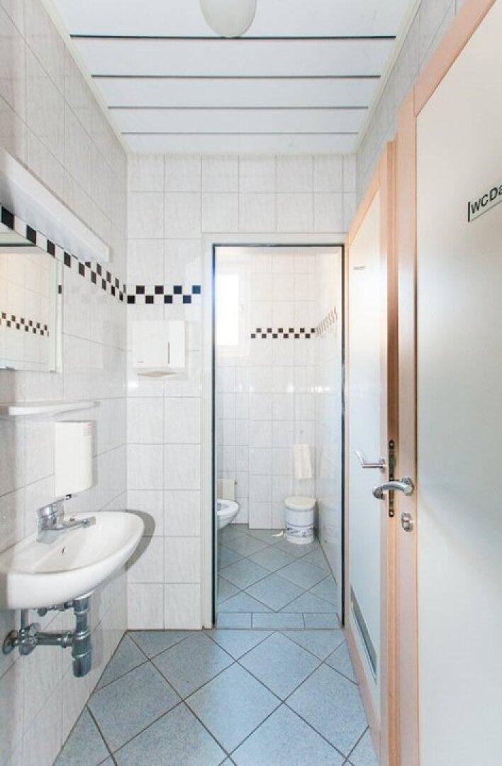 Gefliestes Badezimmer mit Waschbecken, Spiegel und separater Toilettenkabine.