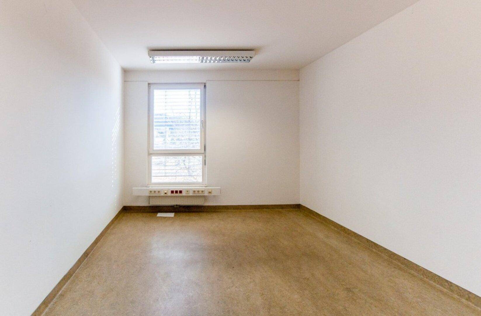 Helles Büro mit einem Fenster, Linoleumboden und Deckenleuchten.