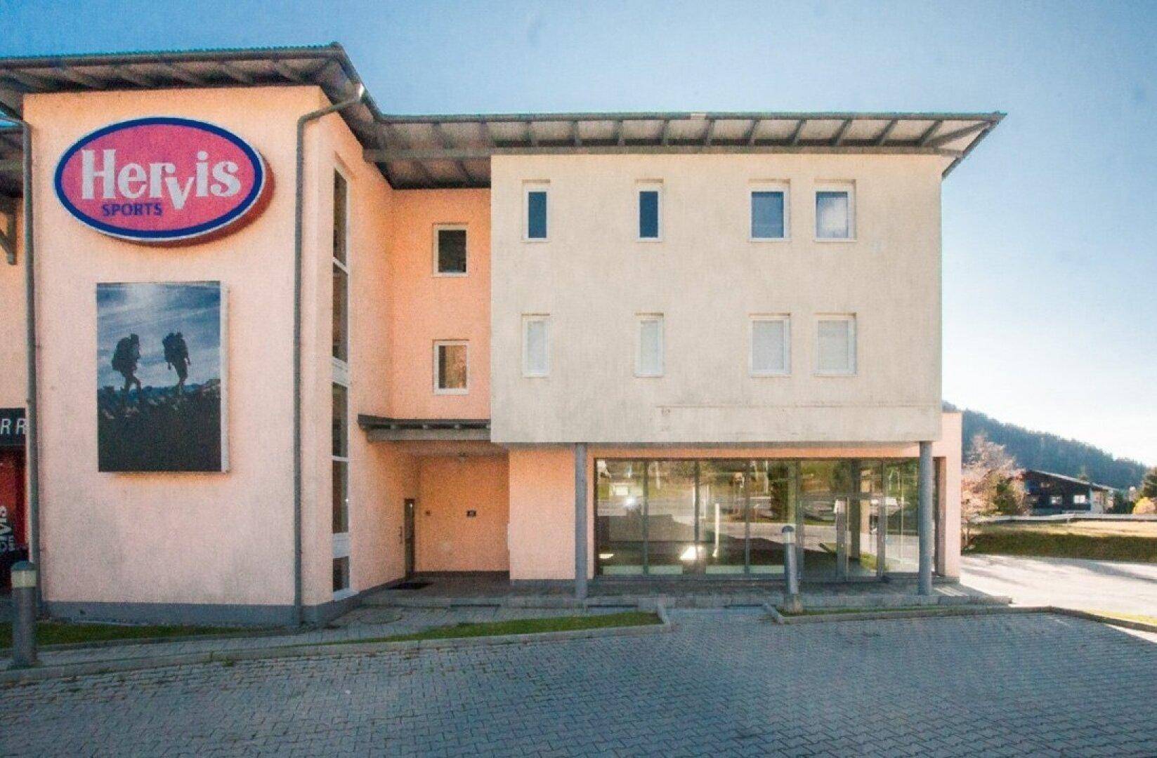 Seitenansicht des Gewerbegebäudes mit großem Hervis Sports Logo und Parkflächen.