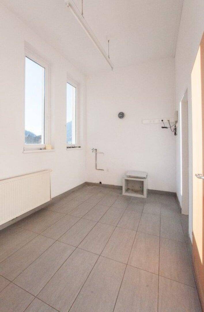 Kleinerer Raum mit Fliesenboden, weißen Wänden, Heizkörper und zwei Fenstern.