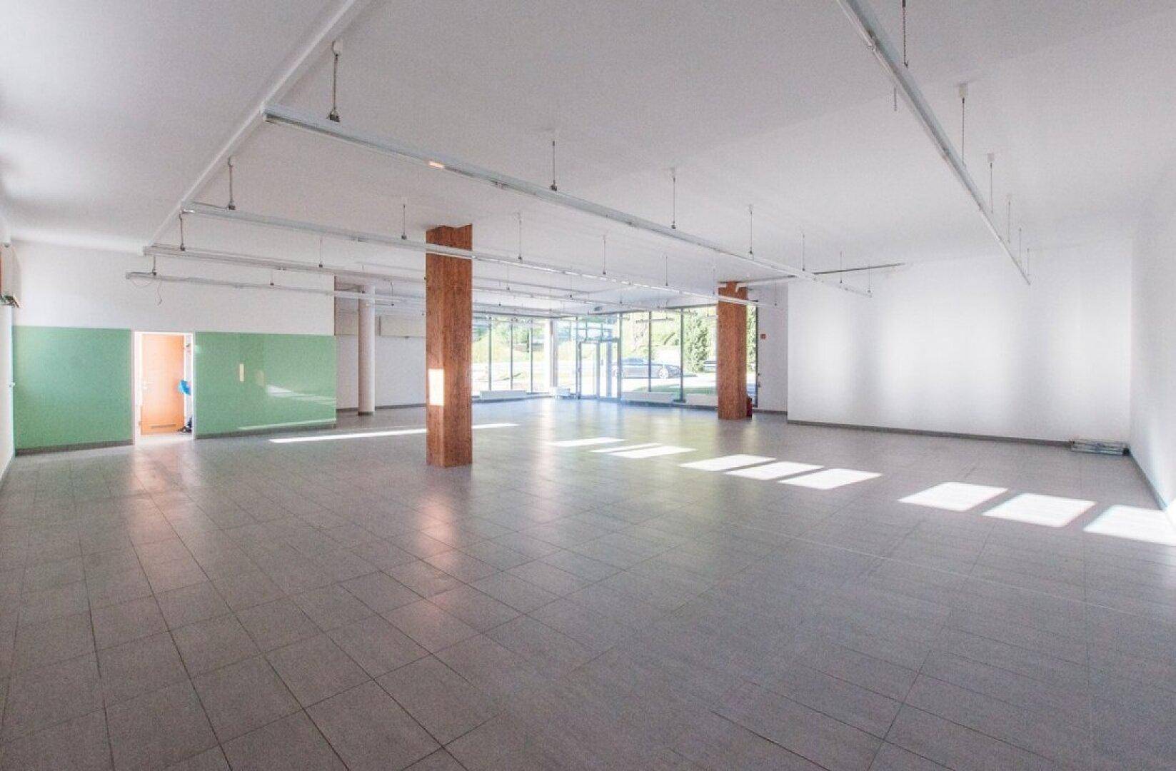 Weitläufiger Gewerberaum mit großen Fenstern, Fliesenboden und Holzsäulen.