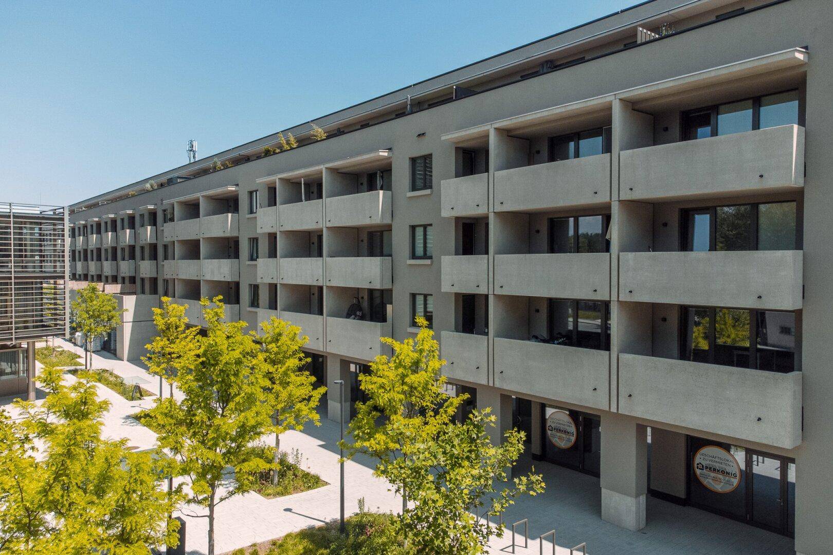 Fassade eines modernen Wohngebäudes mit zahlreichen Balkonen und Geschäften im Erdgeschoss.