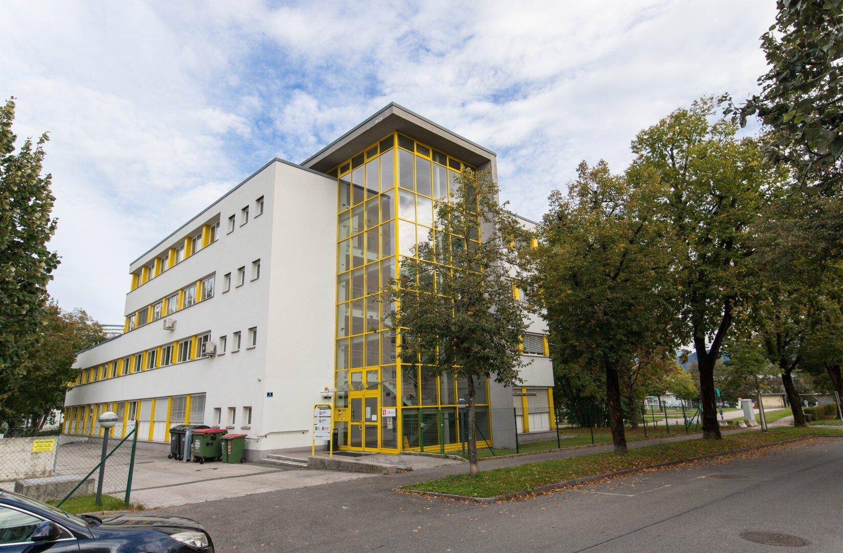 Außenansicht des Bürogebäudes mit markanter gelber Glasfassade und umliegender Grünfläche an einem bewölkten Tag.