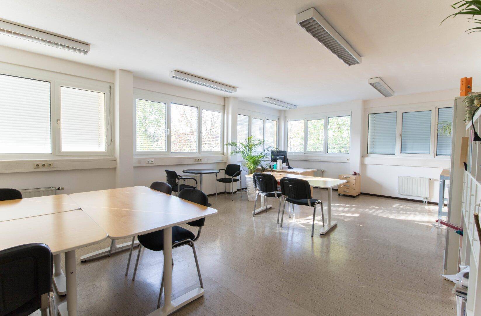 Großes Büro oder Besprechungsraum mit Linoleumboden, vielen Fenstern und mehreren Tischen und Stühlen.