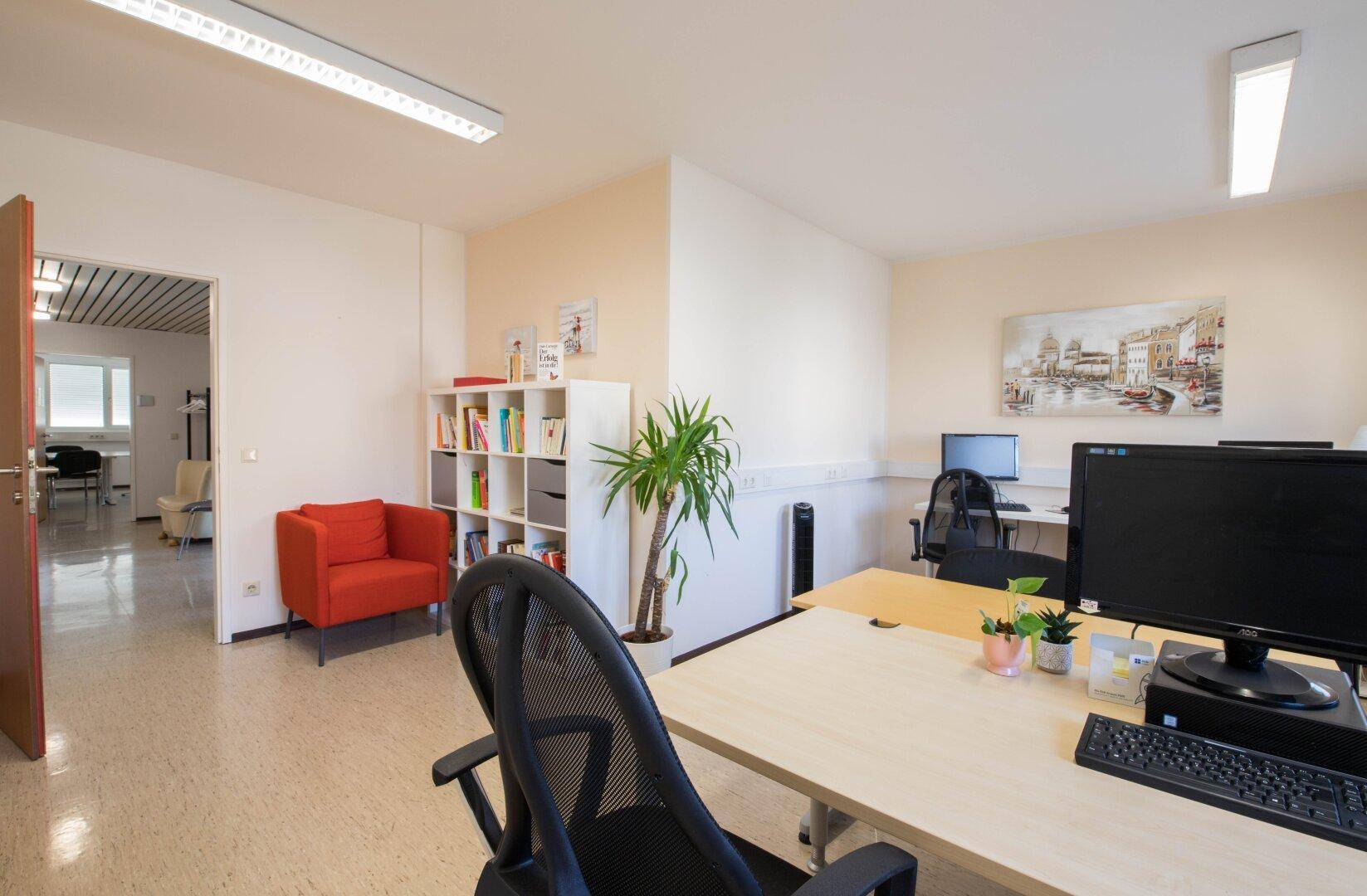 Modern eingerichtetes Büro mit Linoleumboden, weißer Wand und einem Arbeitsplatz, angrenzend an einen weiteren Raum.