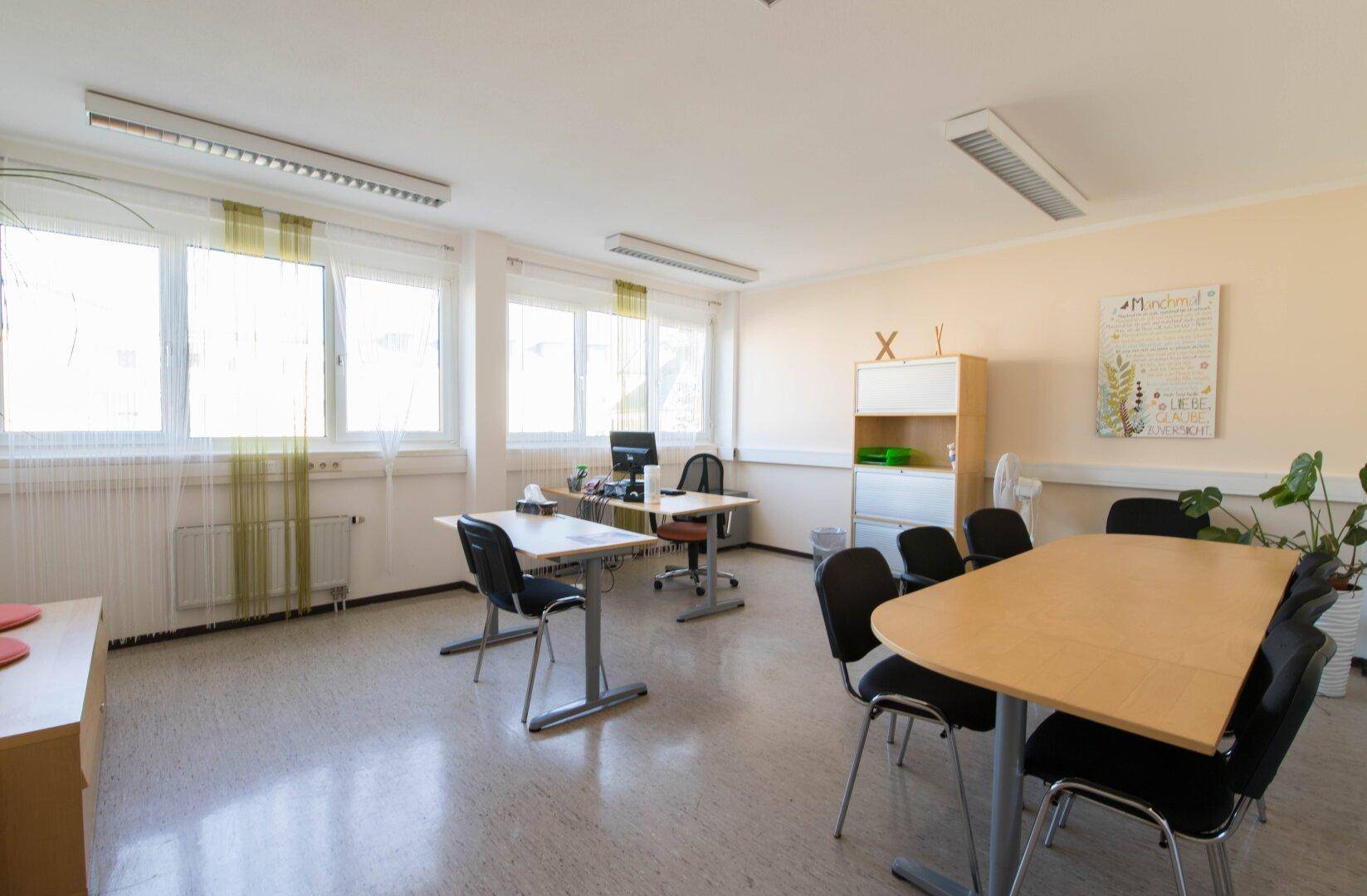 Helles Büro mit Linoleumboden, vielen Fenstern und mehreren Arbeitsplätzen, ausgestattet mit modernen Möbeln.