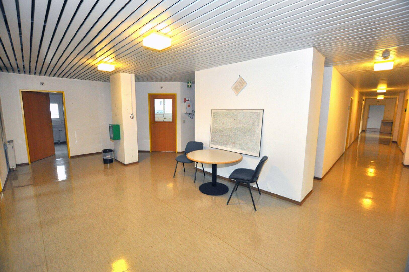 Heller Flur mit Linoleumboden, Sitzgelegenheiten und Zugang zu weiteren Räumen in einem Bürogebäude.