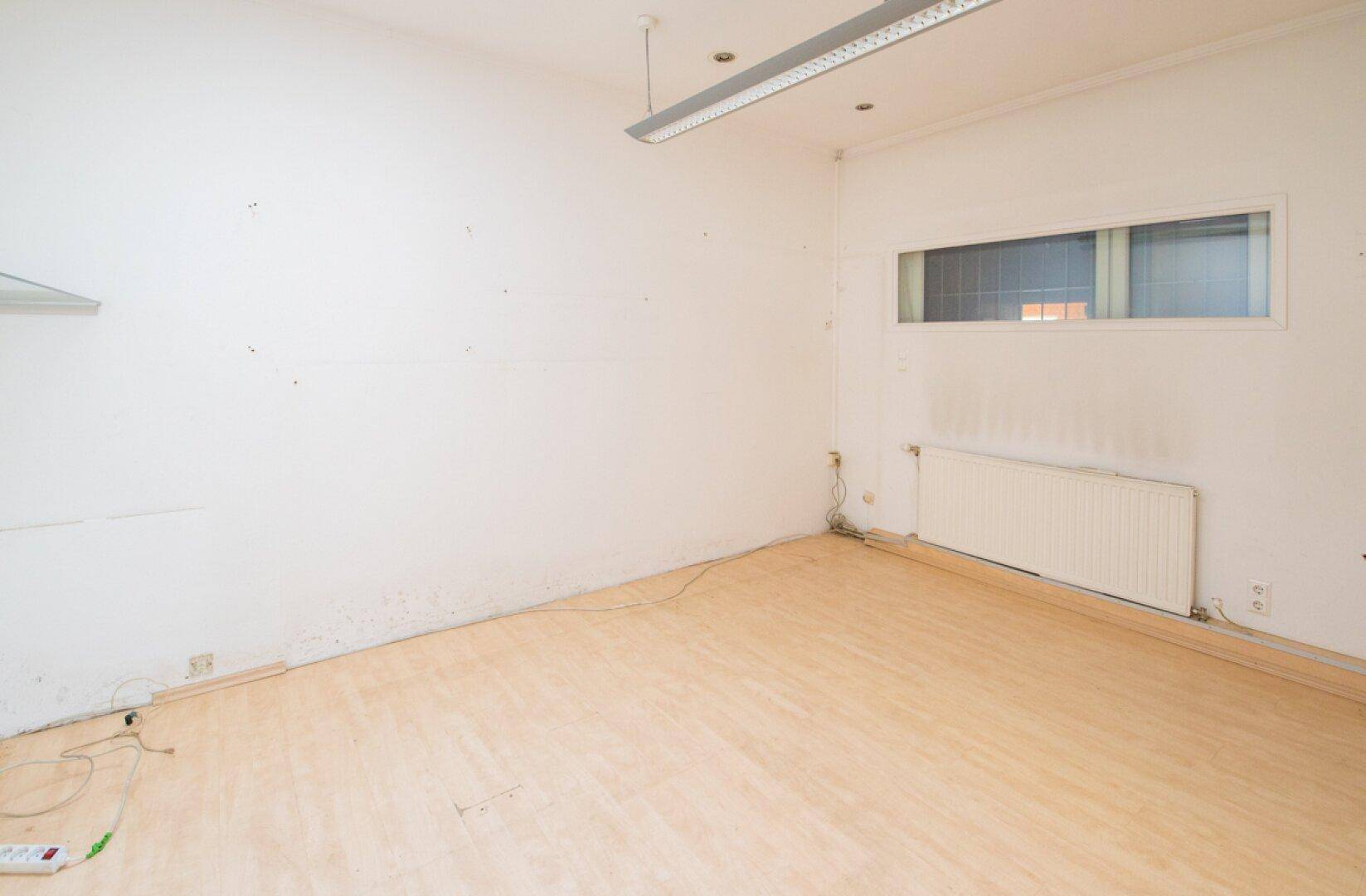 Einfaches Büro mit Laminatboden und Heizkörper, ideal für eine funktionale Arbeitsplatzgestaltung.