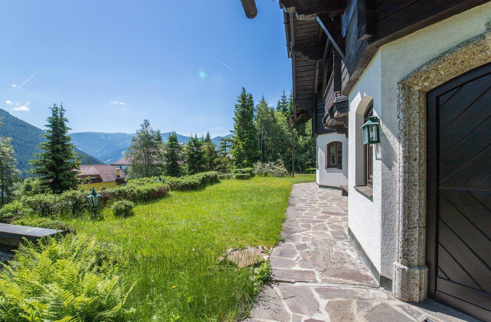 Seitlicher Gartenbereich des Chalets mit Natursteinweg und Blick auf die umliegende Natur und Berge.