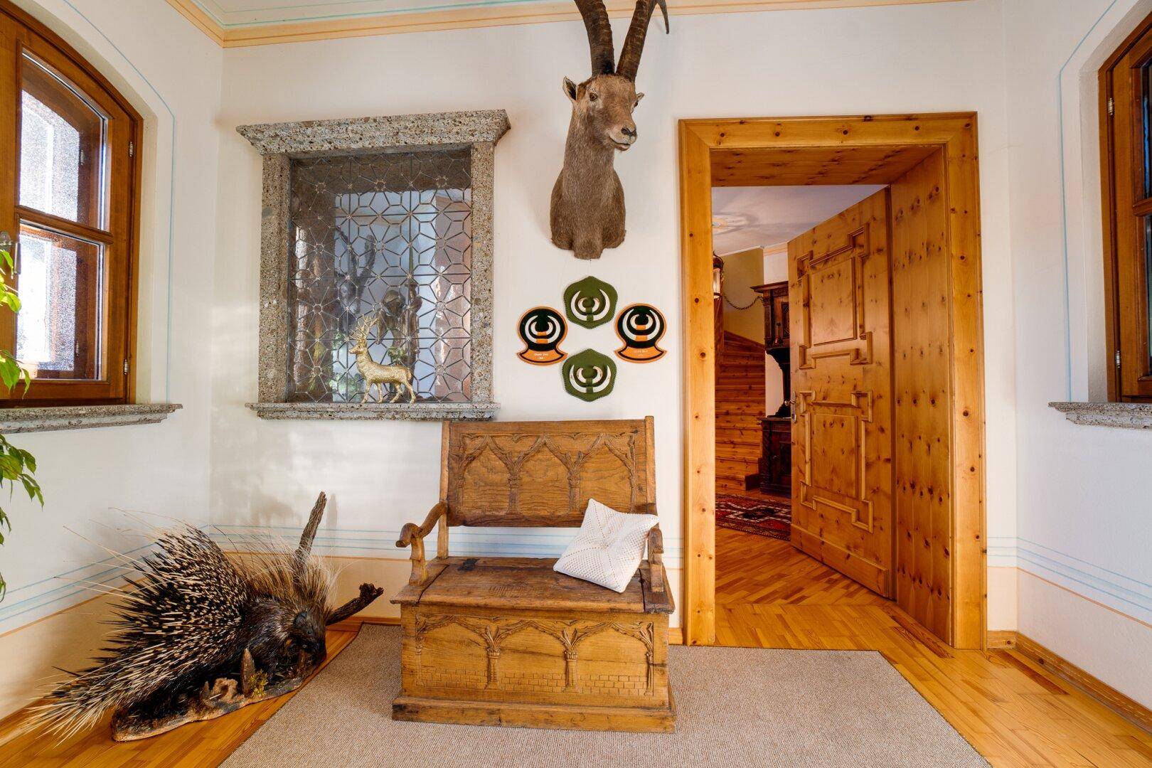 Traditioneller Eingangsbereich mit Holzboden, geschnitzter Bank und alpiner Dekoration, die den Stil unterstreicht.