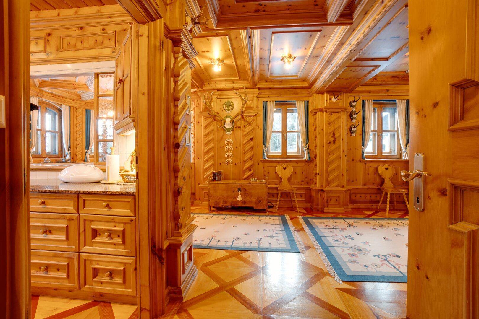 Traditionelles Wohnzimmer im Alpenstil mit aufwendigen Holzvertäfelungen und Parkettboden, der Wärme ausstrahlt.