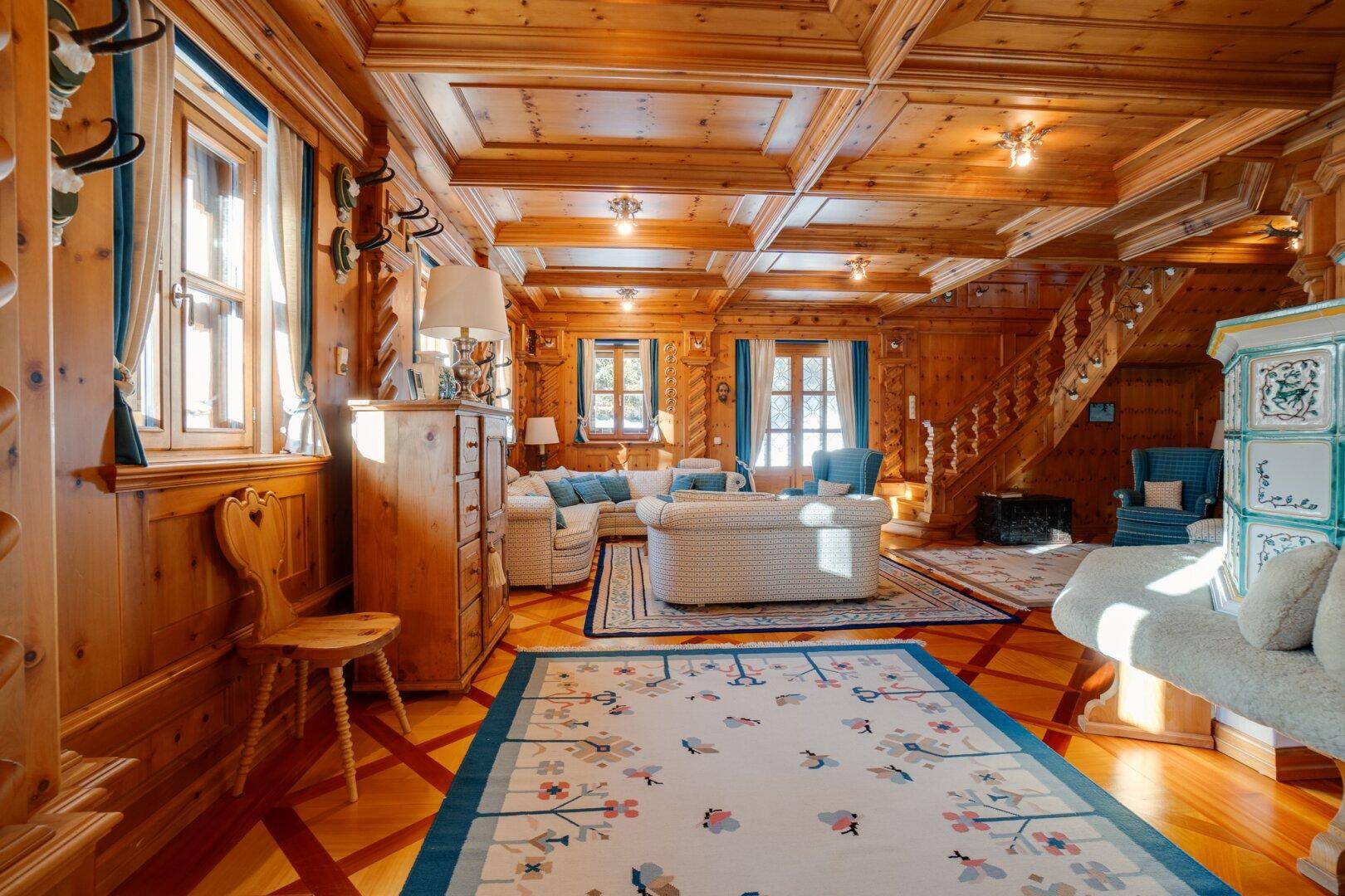 Großzügiges Wohnzimmer mit Holzbalkendecke, gemütlichen Sofas und einem Kachelofen, der zum Verweilen einlädt.