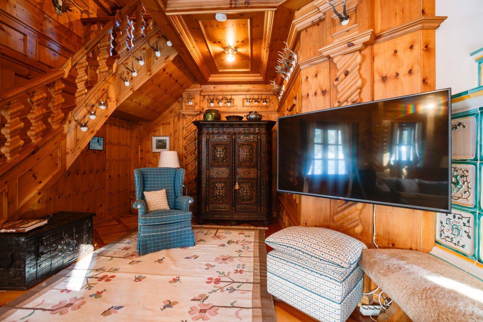 Detailansicht des Wohnzimmers mit Flachbildfernseher, antikem Schrank und alpiner Dekoration, die den Stil unterstreicht.