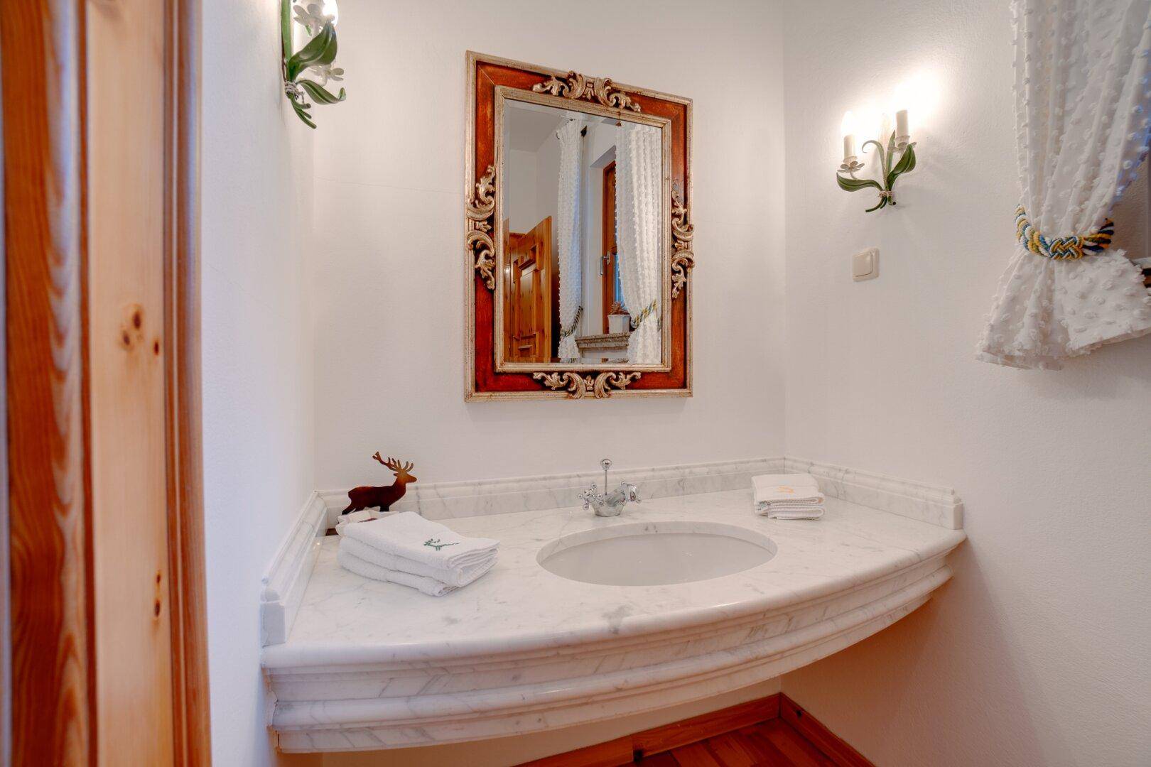 Elegantes Gäste-WC mit Marmorwaschtisch, verziertem Spiegel und traditionellen Armaturen, die Stil verleihen.