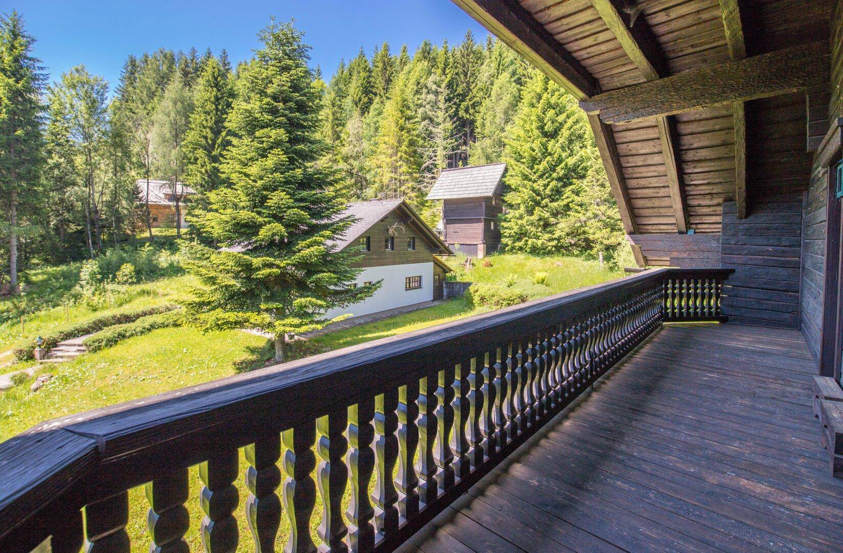 Geräumiger Holzbalkon mit Blick auf die grüne Umgebung und weitere Gebäude, ideal zum Entspannen.