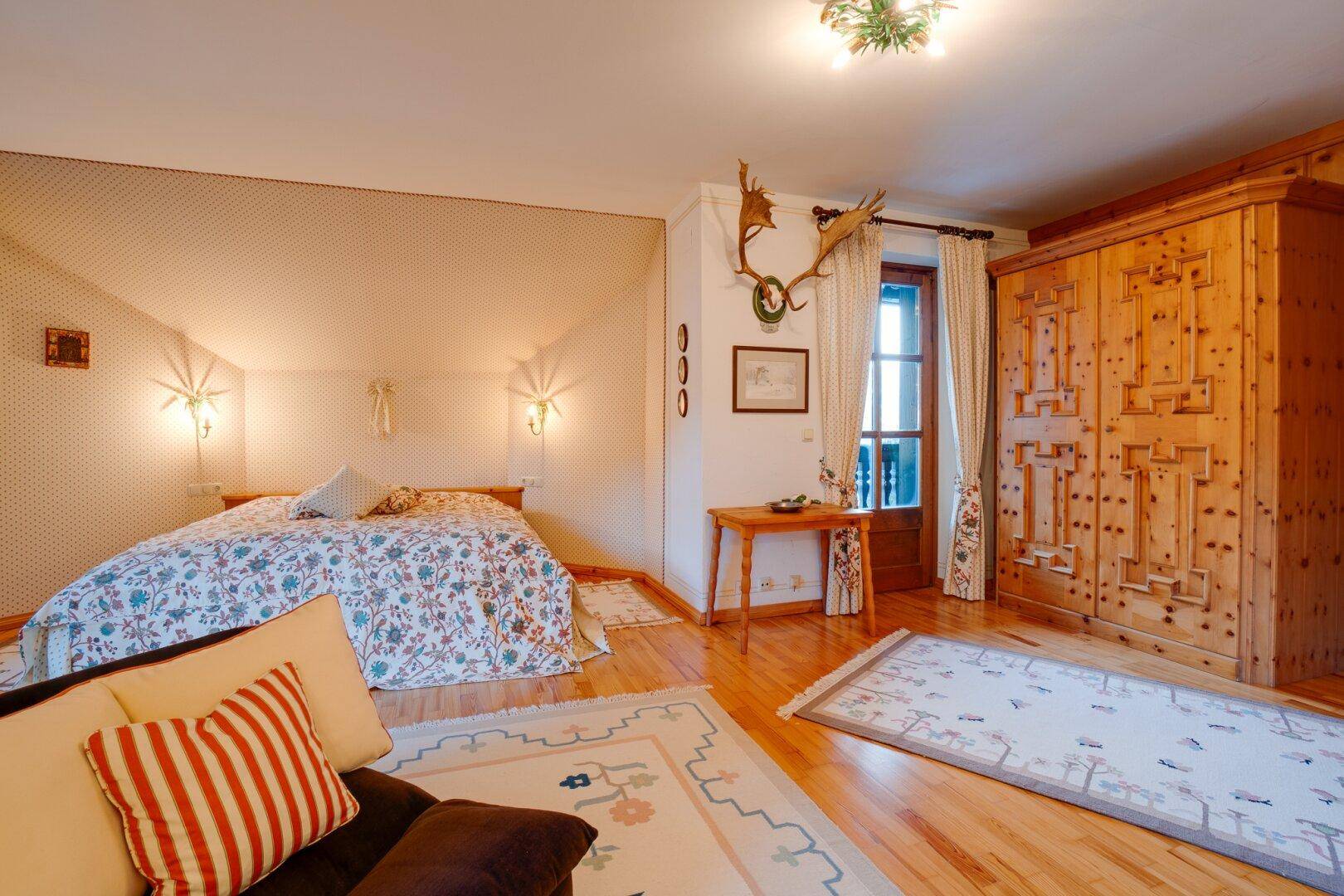 Helles Schlafzimmer mit Doppelbett, Holzboden und traditionellem Kleiderschrank, der viel Stauraum bietet.