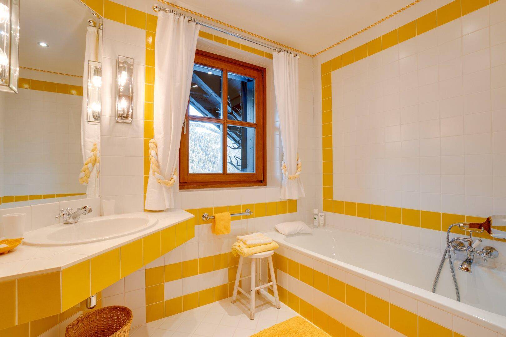 Badezimmer mit Einzelwaschbecken, Spiegel und gelb-weißen Fliesen, die eine freundliche Atmosphäre schaffen.