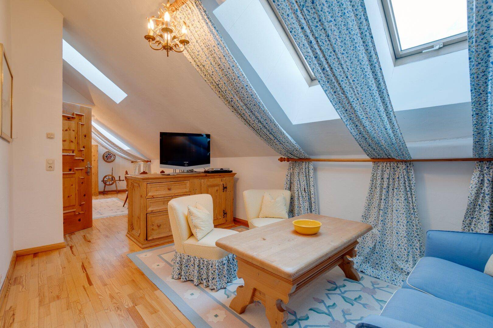 Schlafzimmer im Dachgeschoss mit Holzboden, Dachfenstern und floralem Bettzeug, das eine romantische Note verleiht.