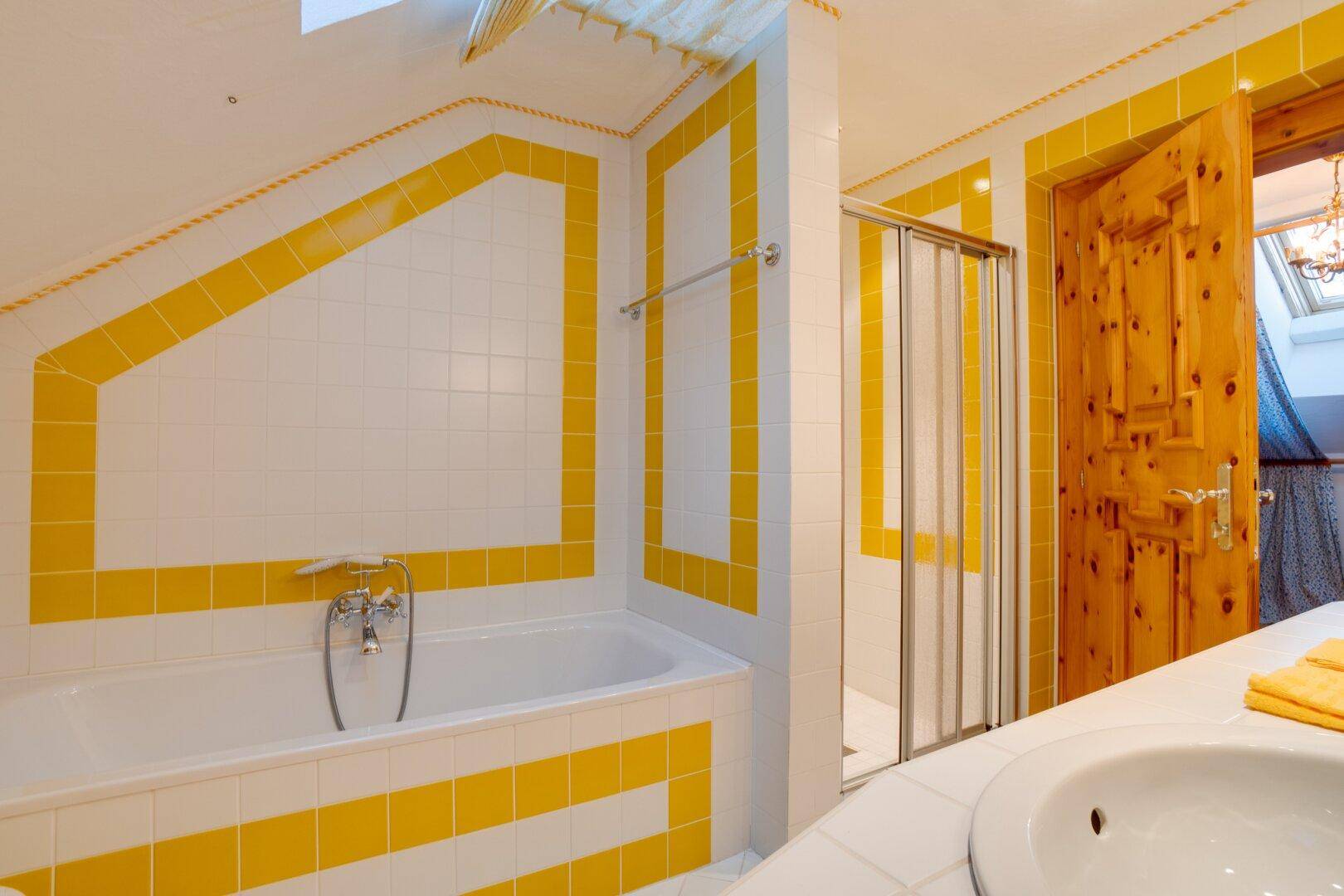 Dachgeschoss-WC mit gelb-weißen Fliesen, Dachschräge und Wand-WC, das den Raum optimal nutzt.