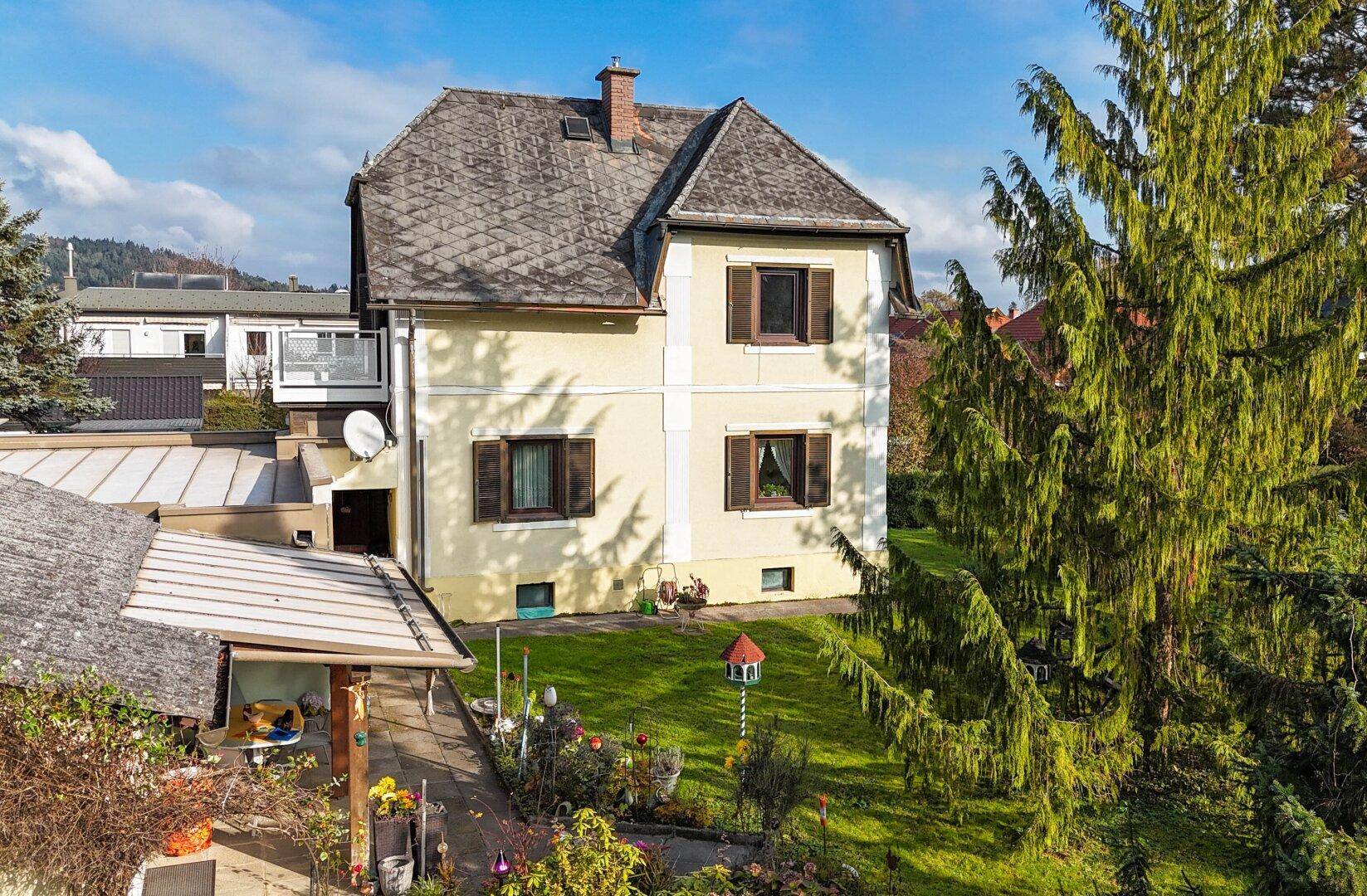 Seitenansicht des Hauses mit traditionellem Dach und einem blühenden Gartenbereich.