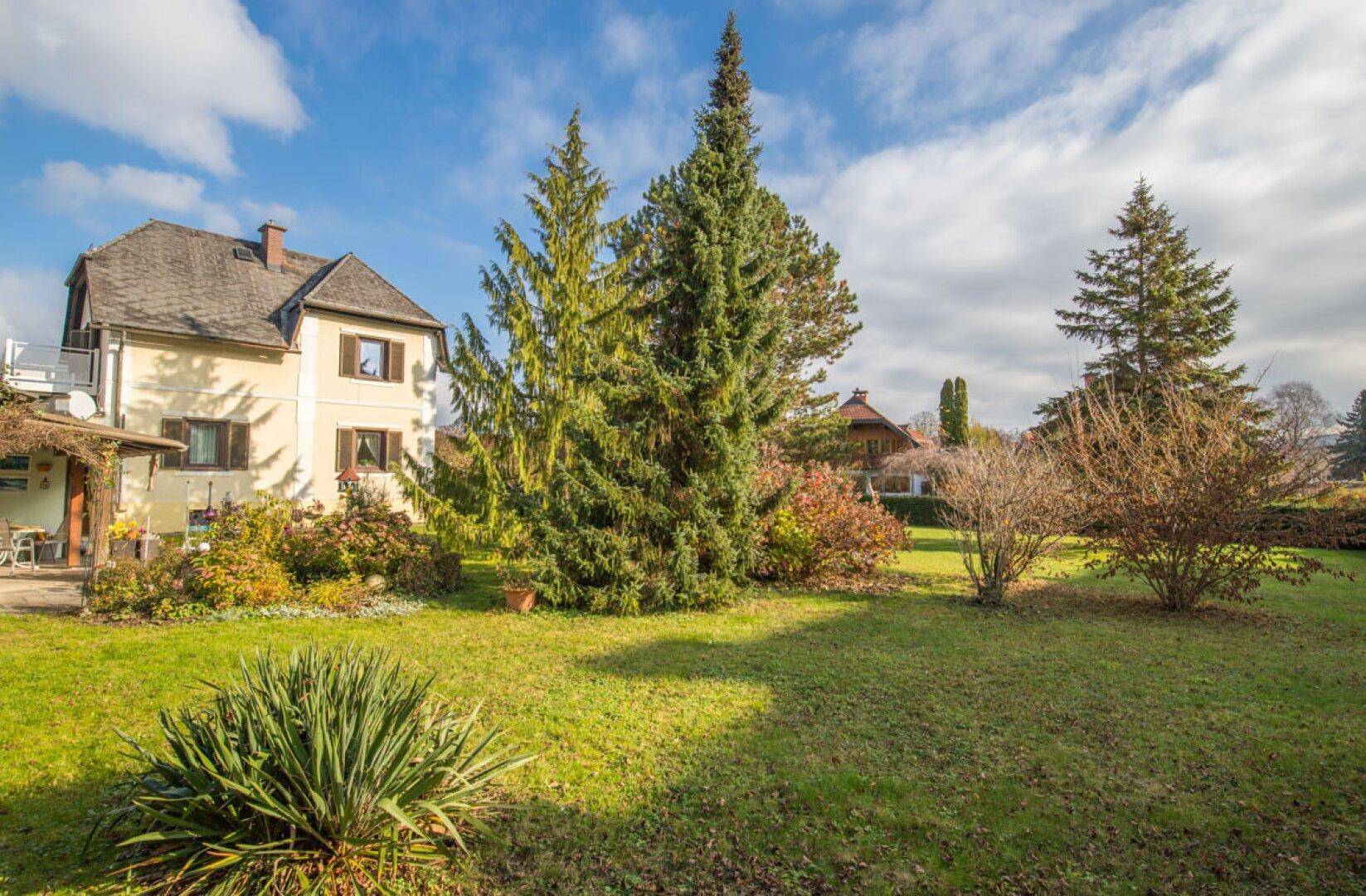 Weitläufiger Gartenbereich mit altem Baumbestand und Blick auf das traditionelle Haus.