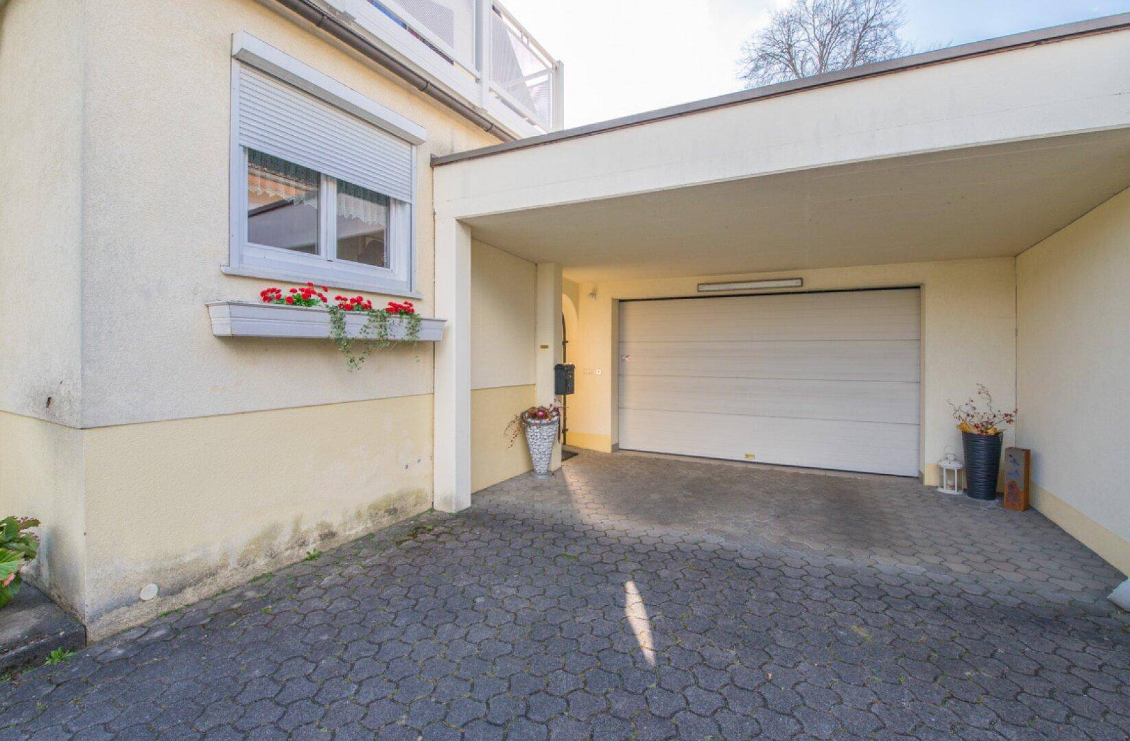 Überdachter Carportbereich mit Garagentor und Fenster mit Rollladen.