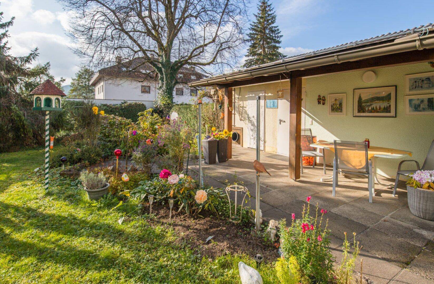 Gemütliche überdachte Terrasse mit Gartenmöbeln und Blick auf den blühenden Garten.