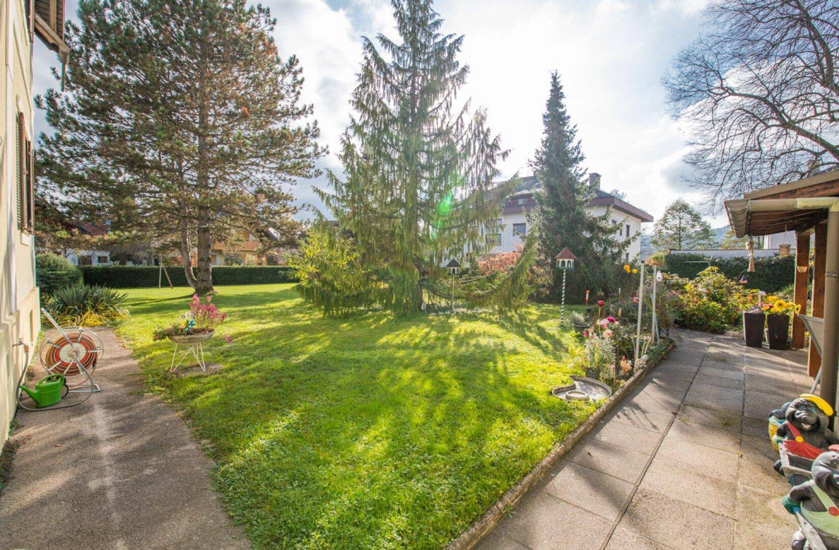Gepflasterter Gartenweg führt durch den grünen Rasen zu blühenden Beeten und Bäumen.