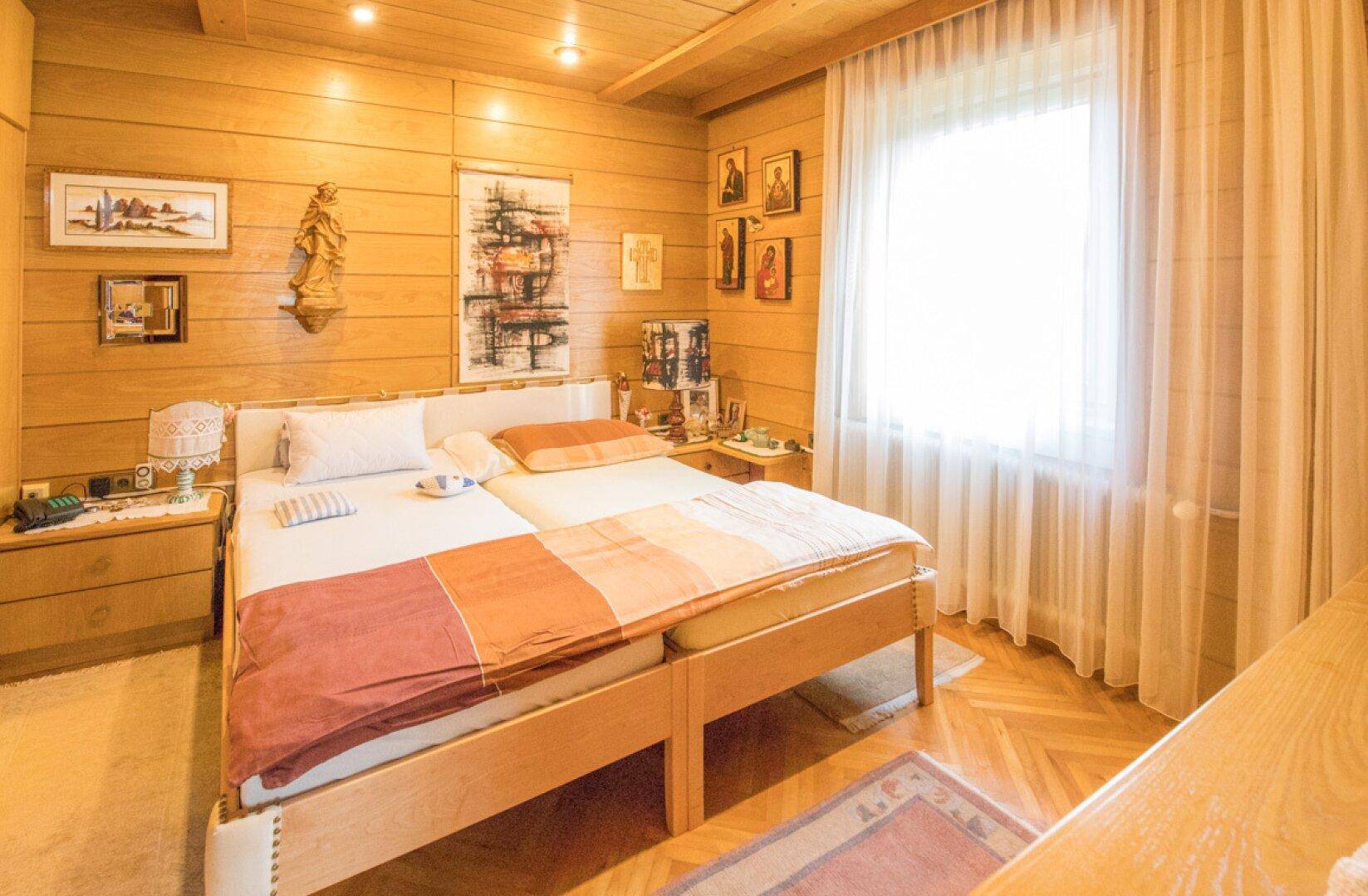 Schlafzimmer mit Holzvertäfelung, Einbauschränken und Blick auf den Wohnbereich.