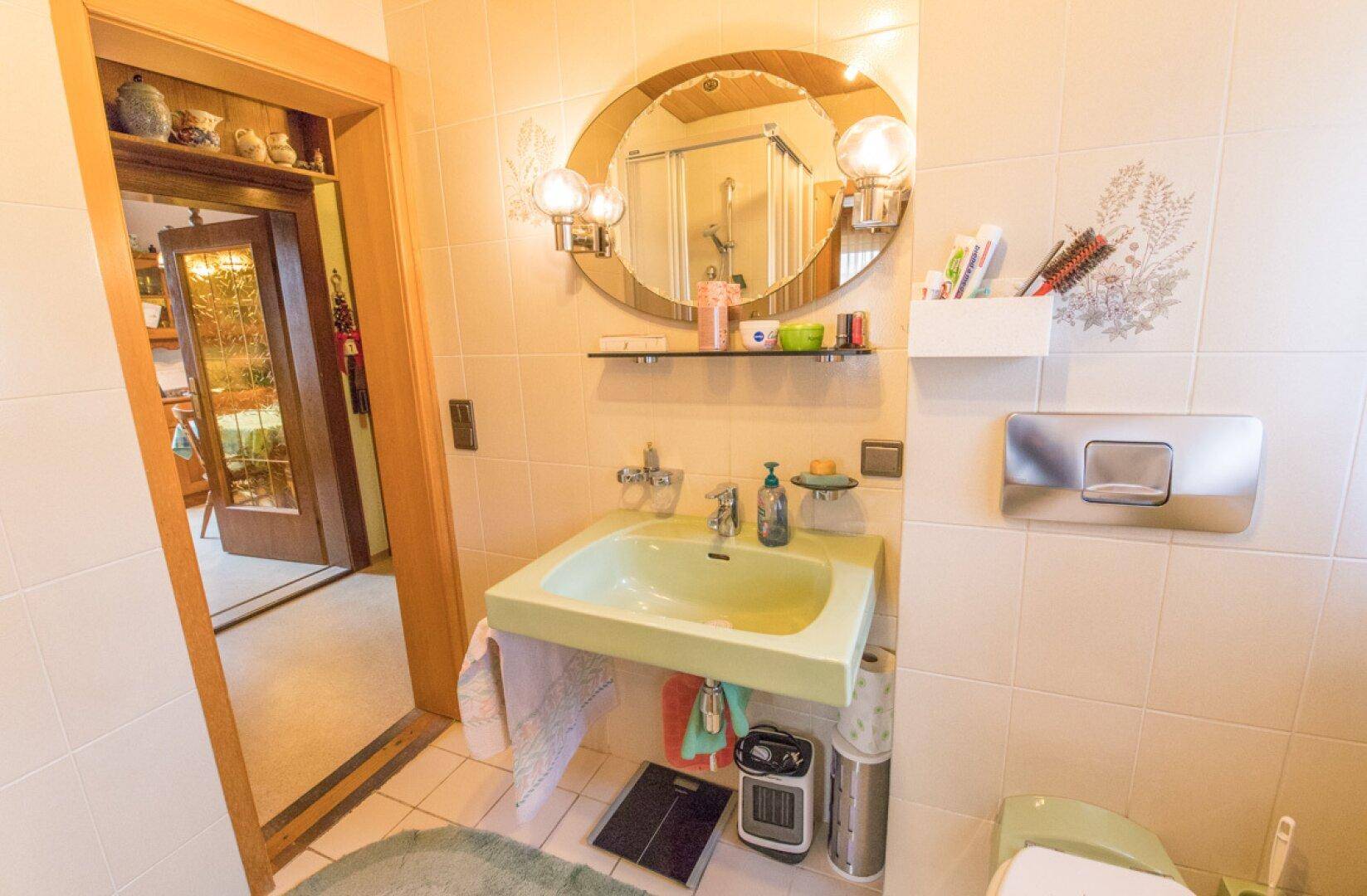 Badezimmer mit Duschkabine, hellen Fliesen und Zugang zu weiteren Räumen.
