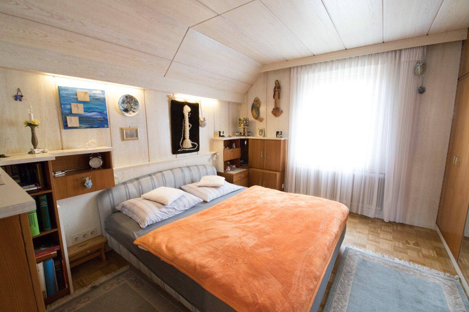 Detailansicht des Schlafzimmers mit Bett, Wanddekoration und Dachschräge.
