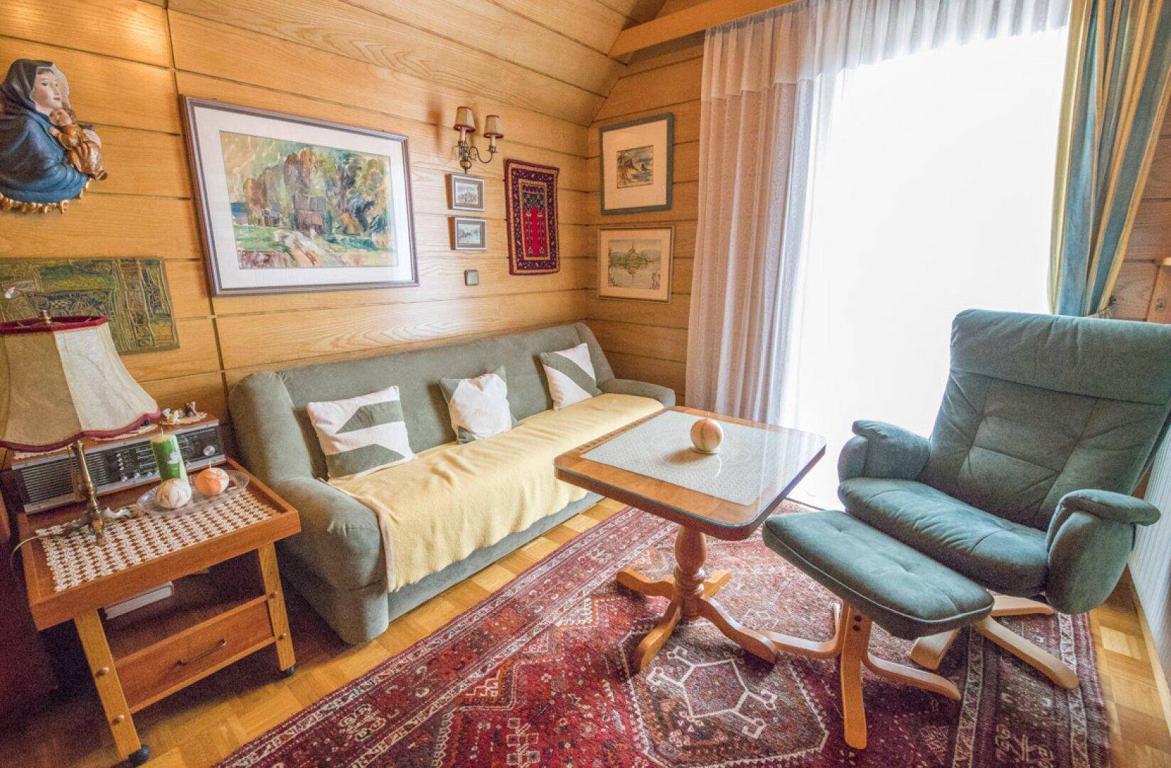 Wohnzimmer mit Holzvertäfelung, Bücherregal und Zugang zu einem weiteren Raum.