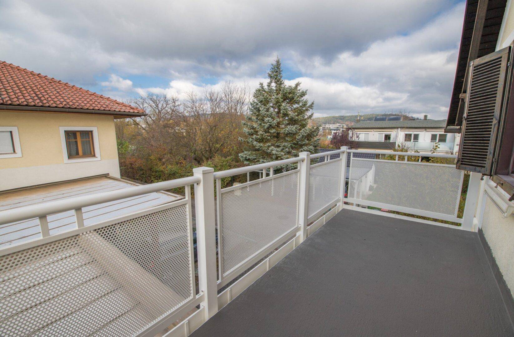Balkon mit Holztür, Fensterläden und Blick auf die Nachbarschaft.